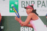 a woman in a pink shirt is holding a tennis racquet in front of a bnp pa sign
