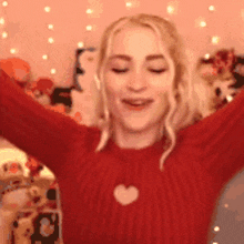 a woman wearing a red sweater with a heart on it is holding her arms in the air .
