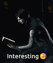 a man with tattoos is reading a book in the dark