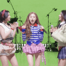 three girls are singing into microphones on a green background