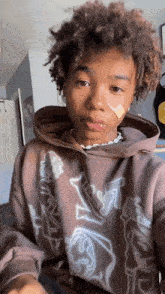 a young man with curly hair and a bandage on his face is wearing a hoodie .