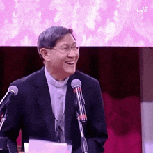 a man in a suit is smiling in front of a microphone with the letters lje behind him