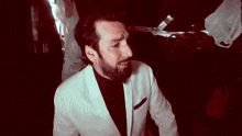 a man with a beard wearing a white suit and black shirt