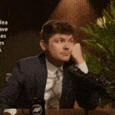 a man in a suit and tie is sitting in front of a microphone with a mug that says af on it