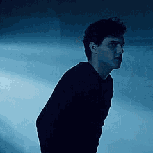 a man in a black shirt is standing in a dark room with a blue background .