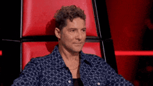 a man with curly hair is sitting in a red chair on a red background .