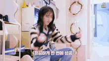 a girl in a striped sweater is sitting on the floor in a room with flowers on the wall .