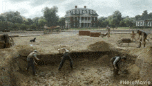a group of men are digging a hole in the dirt in front of a house