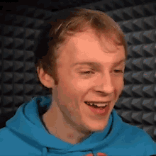 a young man wearing a blue hoodie is smiling in front of a black wall .