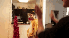 a man in a yellow hoodie is standing next to a red christmas tree