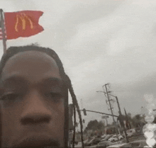 a man with dreadlocks is taking a selfie with a mcdonald 's flag flying in the background .