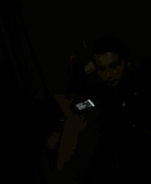 a man in a black jacket is sitting on a bed holding a cell phone