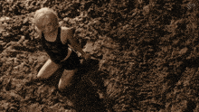 a woman in a black tank top is kneeling in the dirt next to a man laying on the ground
