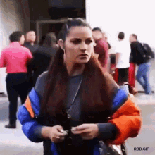 a woman wearing a blue and orange jacket is standing in a crowd of people .