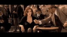 a woman in a black dress is sitting at a table smoking a cigarette