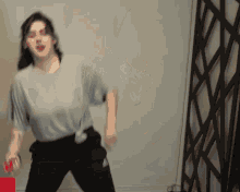 a woman in a grey shirt and black pants is holding a red object