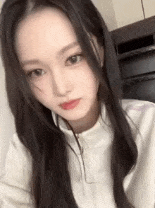 a close up of a woman with long black hair wearing a white jacket and looking at the camera .