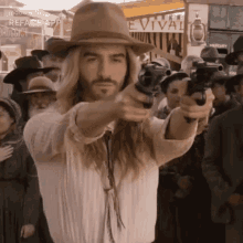 a man with long hair and a hat is pointing a gun at the camera .