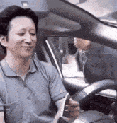 a man is sitting in the driver 's seat of a car holding a piece of paper and smiling .