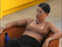 a woman wearing glasses sits in a chair with a blue bottle