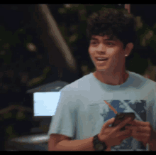 a young man in a blue shirt is holding a cell phone in his hand .