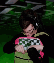 a man wearing glasses and headphones is holding a pink and green checkered bag