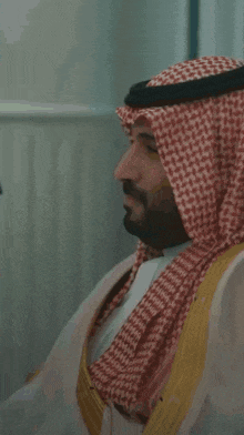 a man wearing a keffiyeh and a robe is sitting in a chair .