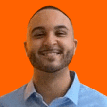 a man with a beard is smiling and wearing a blue shirt against an orange background .