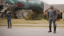 a man and a woman are standing in front of a house with a space ship in the background