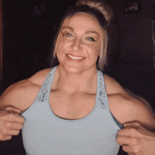 a woman in a blue tank top is smiling with her hands on her chest
