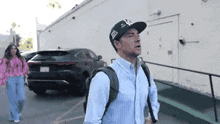 a man wearing a hat and a backpack is standing next to a woman in a pink shirt .