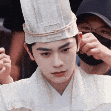 a man wearing a white hat with a rope around it looks at the camera