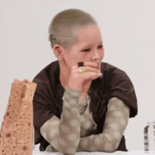 a woman with a shaved head sits at a table with her arms crossed
