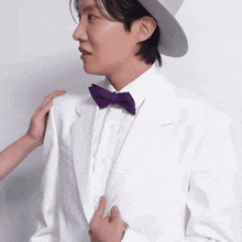 a man wearing a white suit and purple bow tie