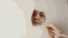 a hand is holding a brush and painting a woman 's face with the words made in animotica behind it