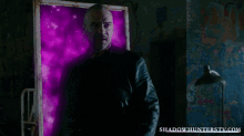 a man in a black suit is standing in front of a purple wall with shadowhunterstv.com written on it