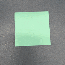 a green square piece of paper is laying on a black surface