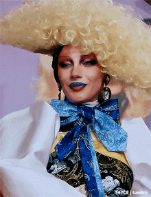a woman wearing a wig and a blue scarf has the tumblr logo on the bottom left