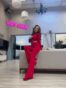 a woman in red sits on a couch in front of a sign that says votana