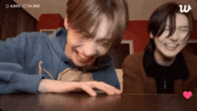 two young men are sitting at a table laughing and one has a heart on the table