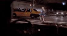 a woman in a blue raincoat is standing in front of a yellow car