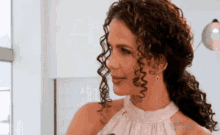 a woman with curly hair is wearing a white dress and earrings