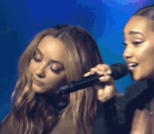 two women are singing into microphones on stage .