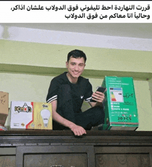 a man sitting on a shelf holding a cell phone next to a box that says dowio