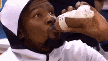 a man is drinking milk from a bottle while wearing a white hooded jacket .