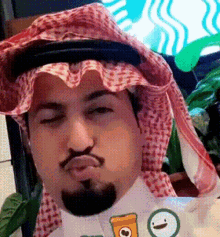 a man with a beard is wearing a head scarf and a starbucks logo on his shirt