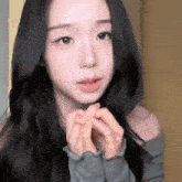 a woman with long black hair is wearing a grey sweater and making a heart with her hands
