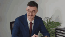 a man in a suit and tie is sitting at a desk and looking at his phone .