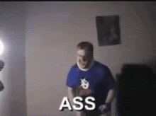 a man in a blue shirt is standing in a dark room with the word ass written on the screen .