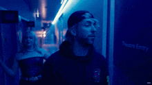a man in a black hoodie stands in front of a blue sign that says theatre entry